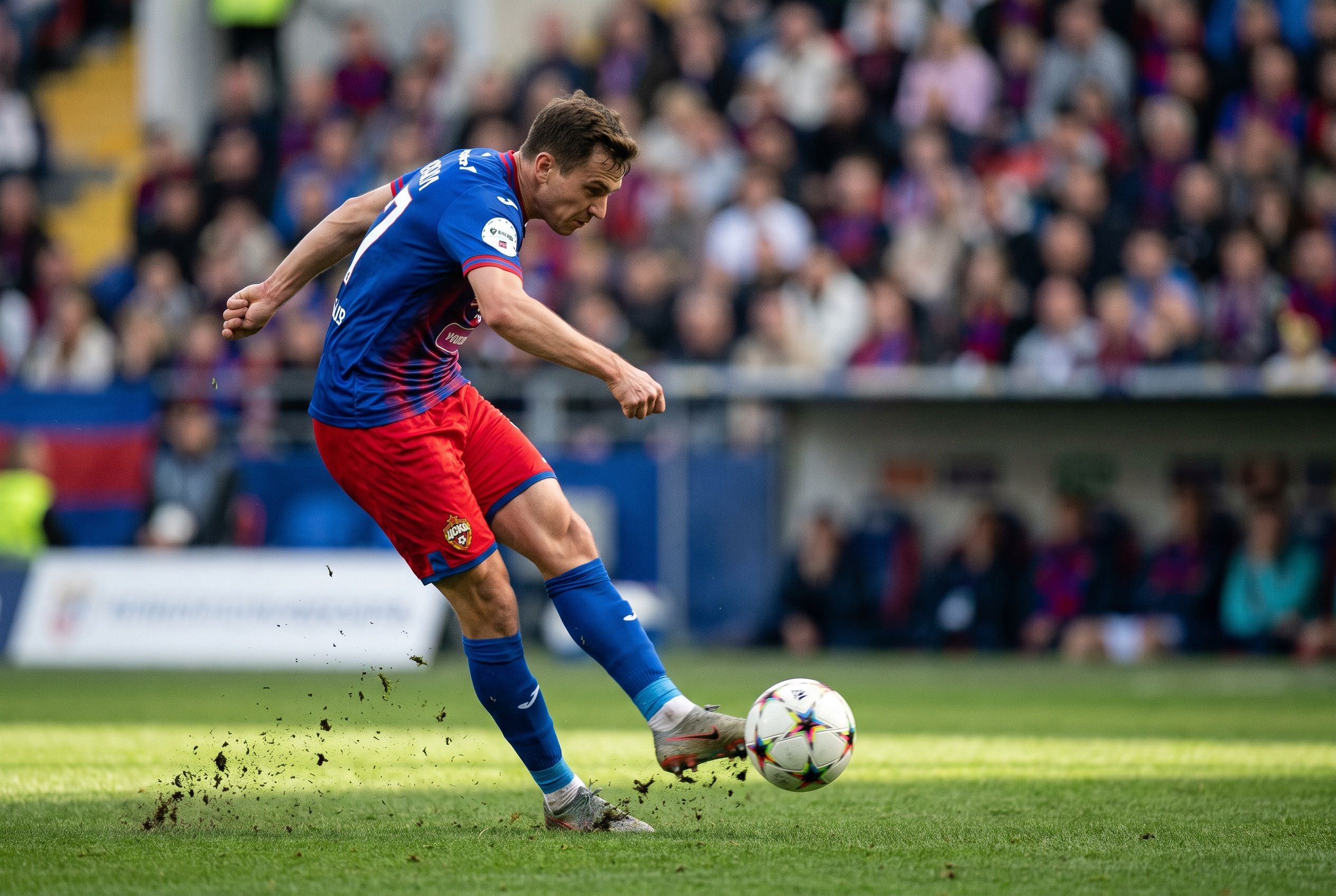 A footballer striking the ball under stadium floodlights, grass spraying up from the pitch