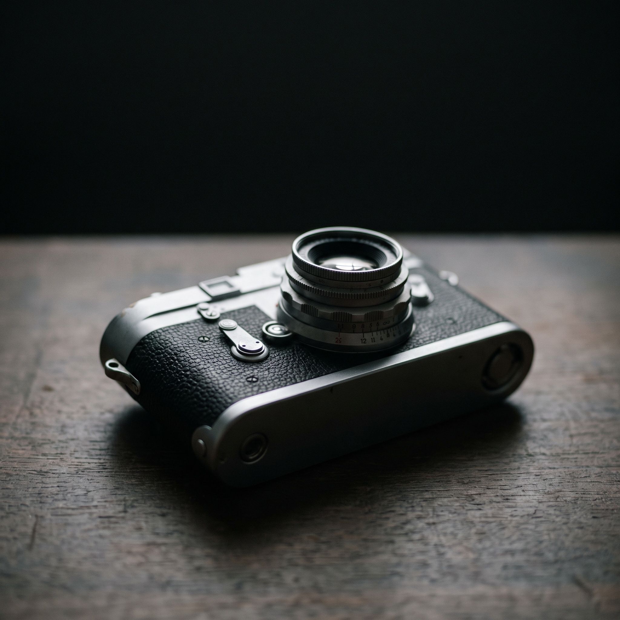 A vintage rangefinder film camera on a weathered wooden table, side light picking out the knurled focus ring